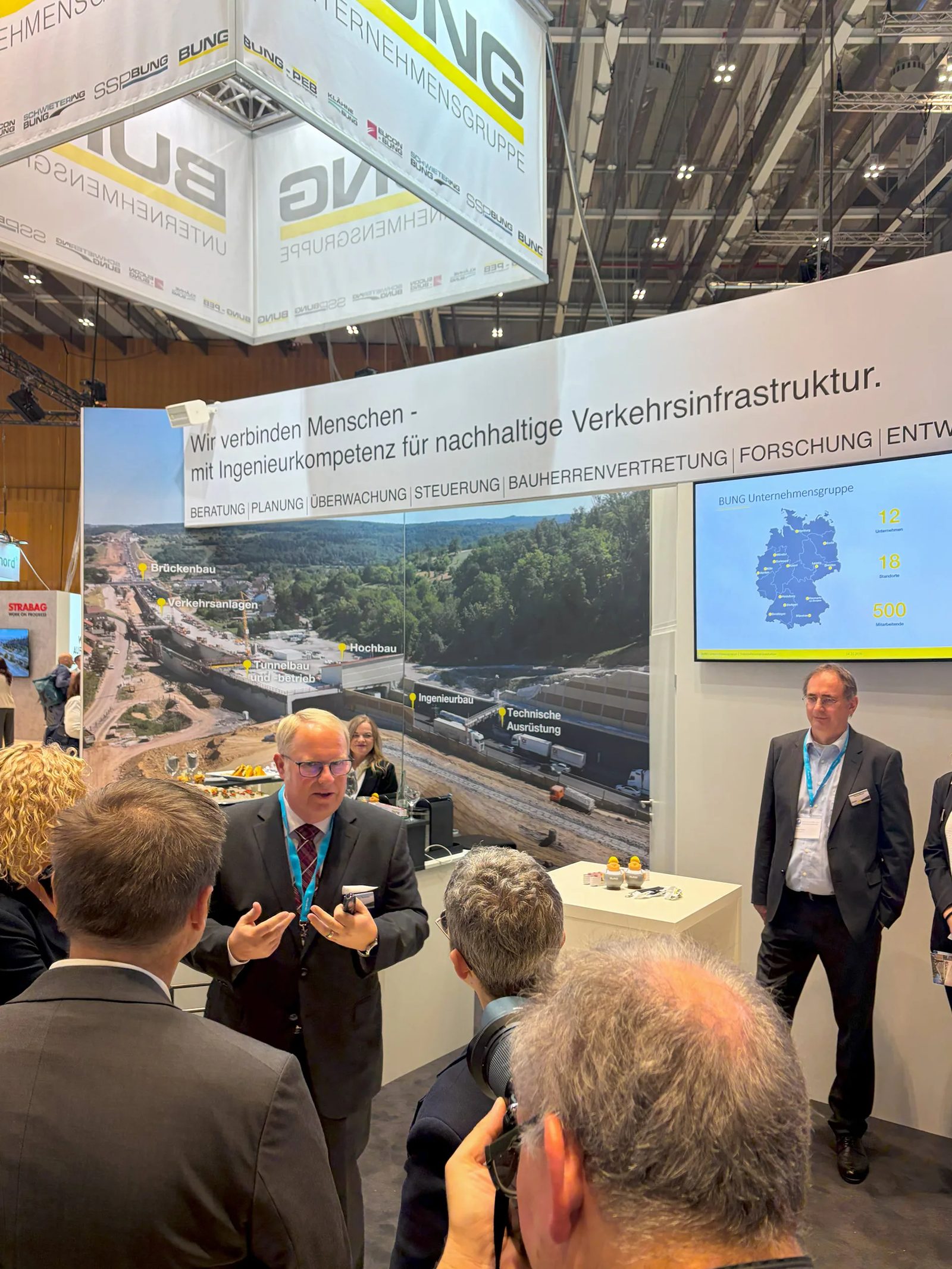 Personen am Messestand der BUNG Unternehmensgruppe auf dem Deutschen Strassen- und Verkehrskongress 2026 in Wiesbaden während der Begrüßung des Ministerrundgangs durch Geschäftsführer Matthias Naewe der BUNG GmbH