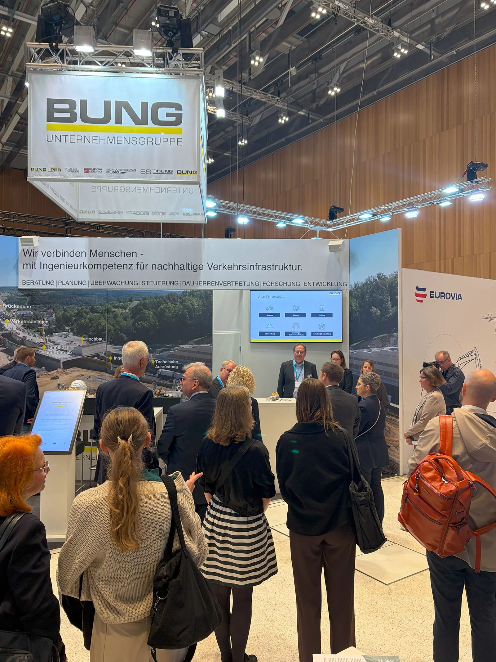 Personen im Gespräch am Messestand der BUNG Unternehmensgruppe auf dem Deutschen Strassen- und Verkehrskongress 2026 in Wiesbaden während eines Vortrages