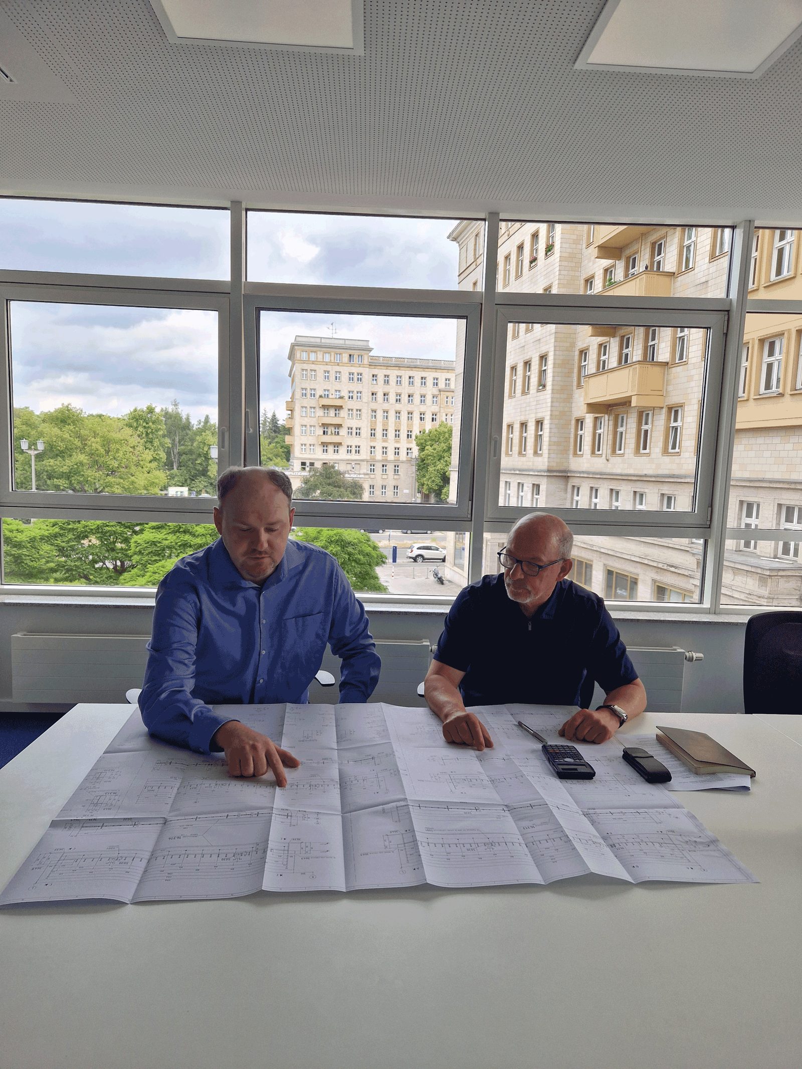 Zwei Ingenieure begutachten großformatige Pläne an einem Besprechungstisch
