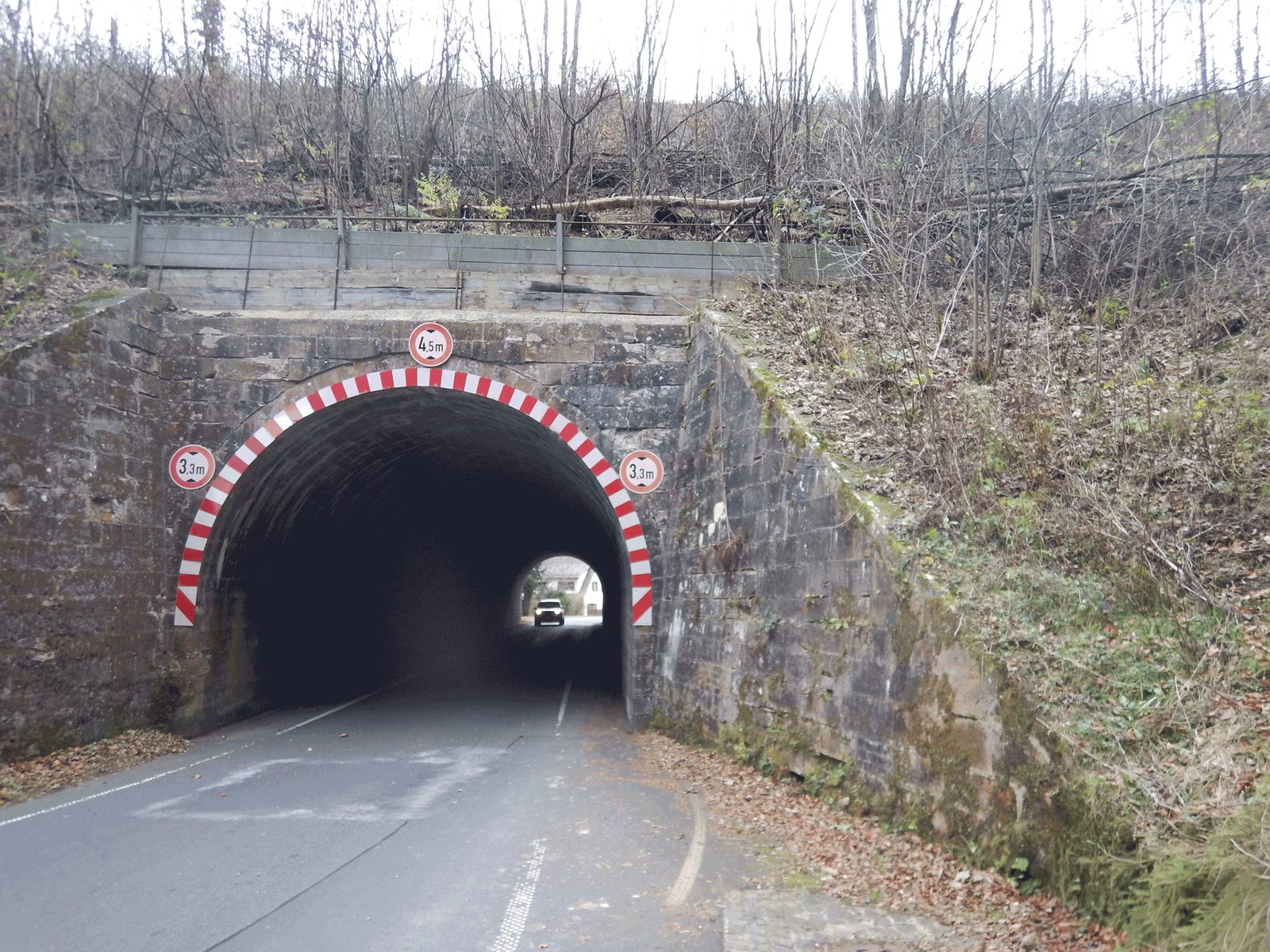 Straße durch eine gemauerte Bogenunterführung mit rot-weißer Höhenmarkierung