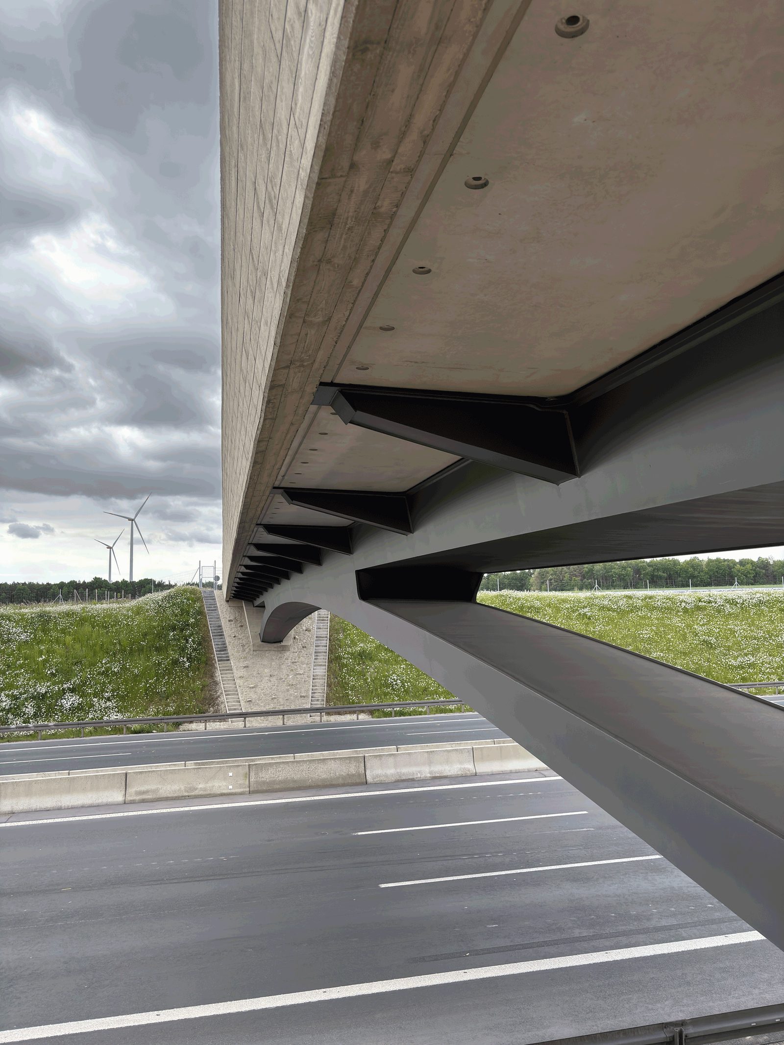 Untersicht eines Brückenüberbaus der A 3 mit Stahlträgern, im Hintergrund Windräder